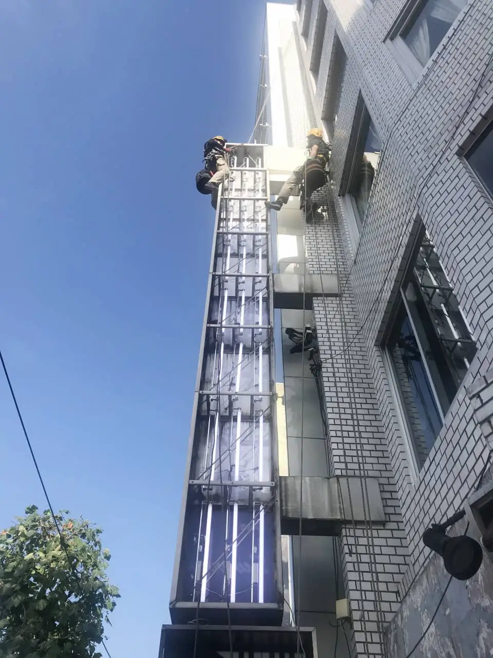 ロープでぶら下がって高所の袖看板で作業する看板職人