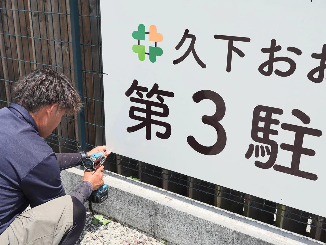 プレート看板をフェンスへ取り付けているところ