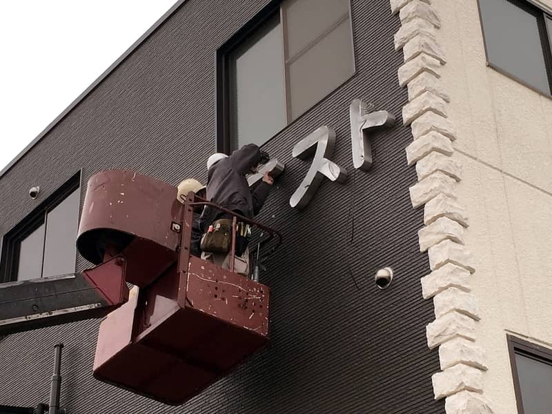 高所作業車で建物の壁面にチャンネル文字を取り付けているところ